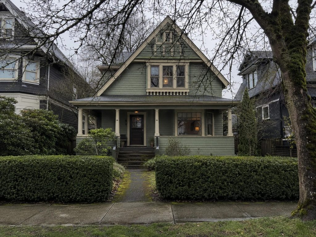 Older Vancouver character house with a deep covered porch and period detailing on a wet residential street